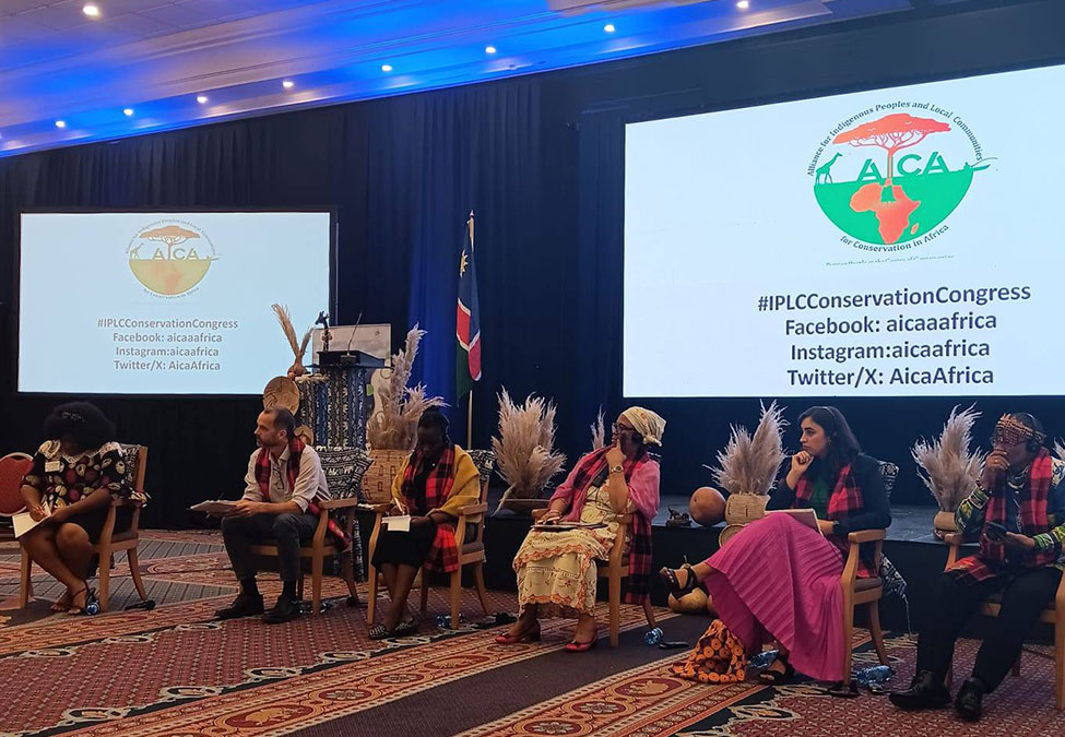 A group of people seated on a stage with a background screen displaying the logo and social media handles for the IPLC Conservation Congress. The screen reads, "IPLCConservationCongress Facebook: aicaafrica Instagram: aicaafrica Twitter/X: AicaAfrica.